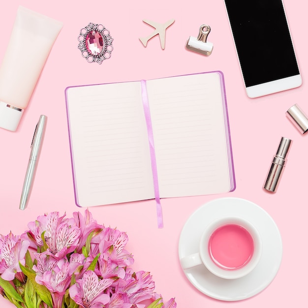 Espace de travail avec agenda, stylo, smartphone, rouge à lèvres, alstroemerias, tasse à thé, cosmétiques