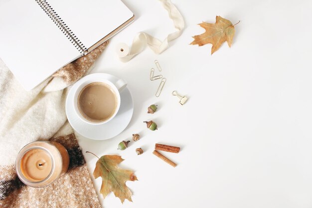 Photo espace de travail d'automne nature morte automne scène féminine scène de maquette de cahier avec tasse de café bougie bâtons de cannelle couverture de laine feuilles de chêne et glands fond de tableau blanc vue de dessus plat