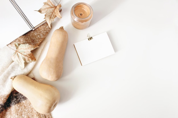 Photo espace de travail d'automne nature morte scène de maquette de cahier et de carte de visite avec couverture en laine feuilles d'automne et citrouilles composition de style féminin d'automne fond de tableau blanc vue de dessus à plat