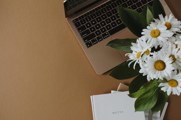 Espace de travail de bureau à domicile esthétique ordinateur portable ordinateur portable bouquet de fleurs de marguerite dans un vase sur une table marron beige neutre Fond de blog de style de vie d'influenceur avec espace de copie