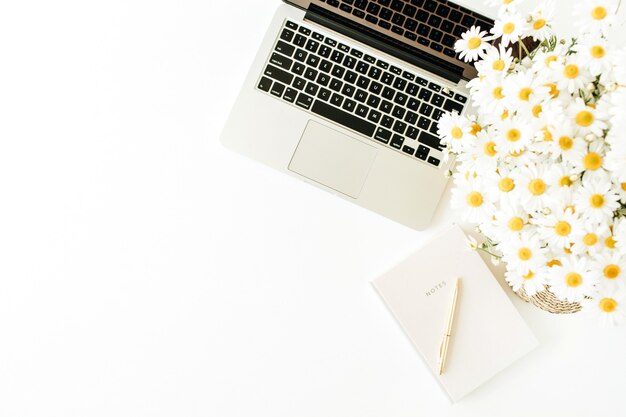 Espace de travail de bureau à domicile avec ordinateur portable, bouquet de camomille et ordinateur portable sur une surface blanche