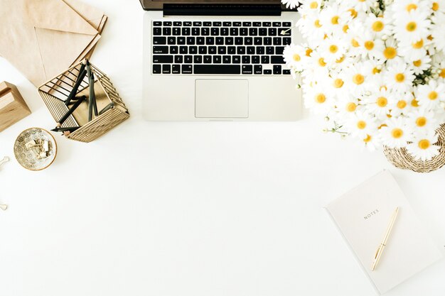 Espace de travail de bureau à domicile avec ordinateur portable, bouquet de fleurs de marguerite de camomille et ordinateur portable sur une surface blanche