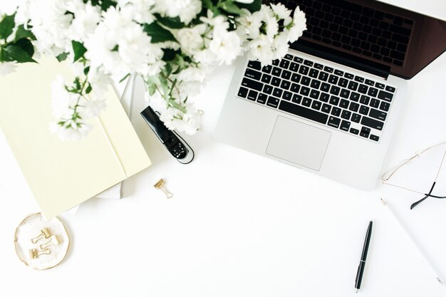 Espace de travail de bureau avec ordinateur portable, bouquet de fleurs et papeterie sur tableau blanc