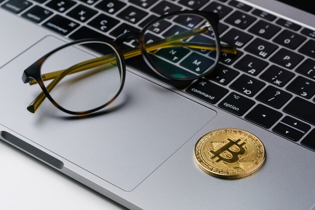 Espace de travail de bureau pièces d'or ordinateur portable Bitcoin, lunettes. Concept de trading de crypto-monnaie Bitcoin