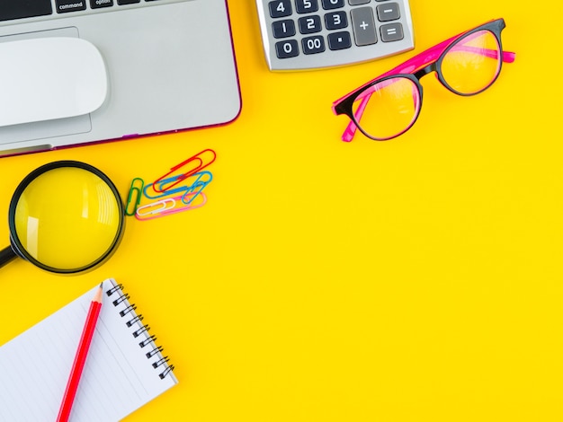 Espace de travail de bureau vue de dessus avec des accessoires de bureau sur fond jaune.