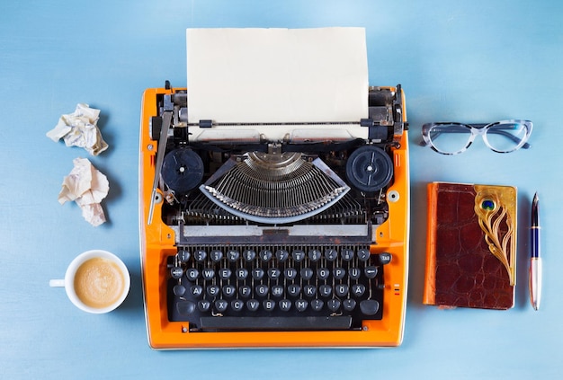 Espace de travail avec un café à machine à écrire vintage orange et un bloc-notes sur fond bleu
