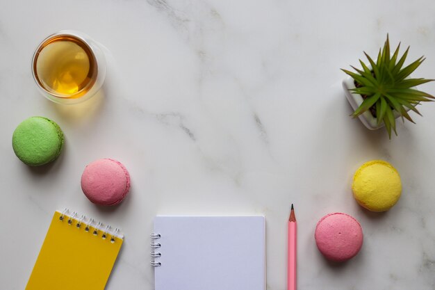 Espace de travail créatif avec cahiers, crayon, plante, tasse de thé et macarons avec espace copie