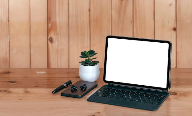 Espace de travail créatif de maquette dans un style vintage avec tablette à écran blanc et clavier magique, smartphone, écouteur et stylo sur une table en bois de planche.