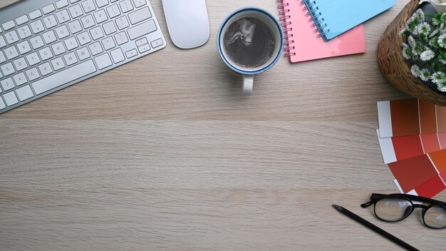 Espace de travail design avec clavier, tasse à café, verres et cahier sur table en bois