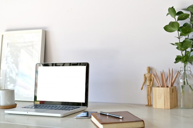 Espace de travail élégant avec ordinateur portable, fournitures créatives, plante d&#39;intérieur et livres au bureau.