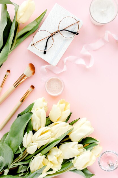Espace de travail féminin avec bouquet de fleurs de tulipes accessoires dorés journal sur fond rose mise à plat wom