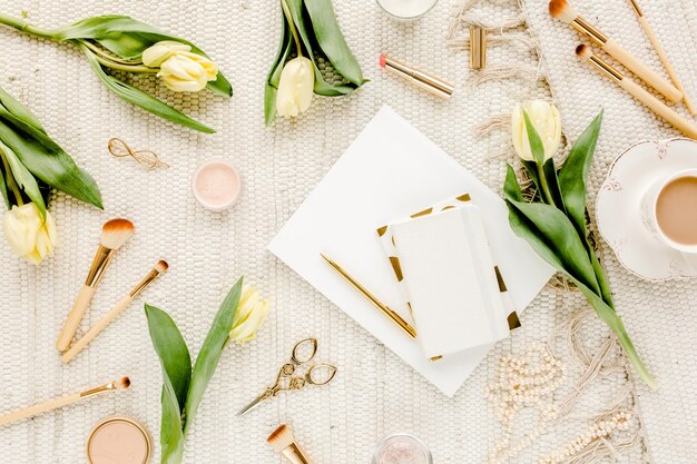 Espace de travail féminin avec fleurs de tulipes jaunes accessoires dorés de mode pour femmes lunettes de journal sur blanc