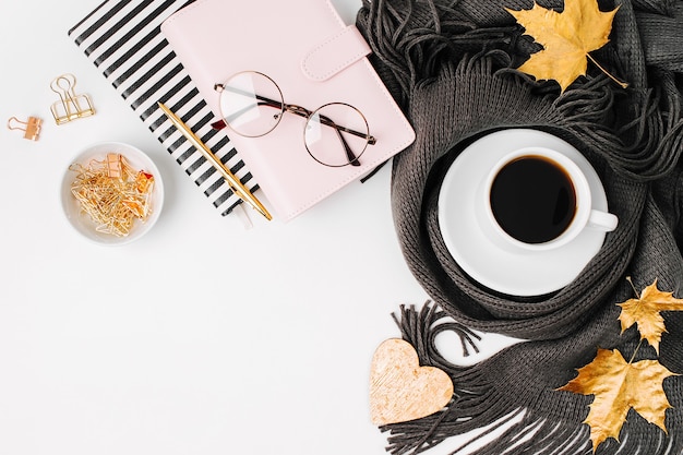 Espace de travail avec feuilles d'érable dorées, cahier, tasse à café enveloppée dans une écharpe, lunettes. Bureau de bureau élégant. Concept d'automne ou d'hiver. Mise à plat, vue de dessus