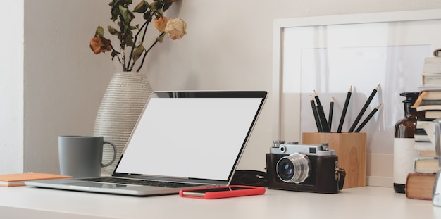 Espace de travail minimal avec ordinateur portable, appareil photo, fournitures de bureau et vase de roses sèches