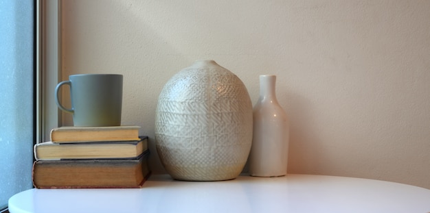 Espace de travail minimal avec des vases en céramique sur une table blanche avec des livres et une tasse de café