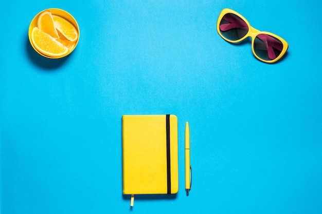 Espace de travail de mode féminine minimaliste élégant. Lunettes et journal jaune vif avec stylo, pirces oranges contre un espace de copie bleu profond. Vue de dessus.