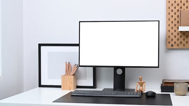 Espace de travail moderne avec ordinateur, cadre photo vide et fournitures de bureau sur tableau blanc.