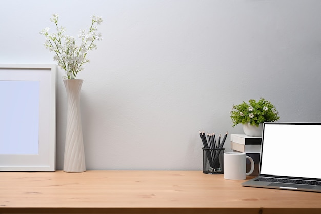 Espace de travail moderne avec ordinateur portable, tasse à café, porte-crayon, livres et plante d'intérieur sur table en bois.