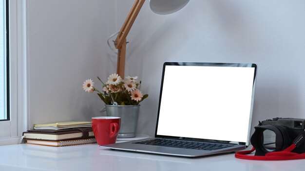 Espace de travail photographe ou concepteur avec ordinateur portable à écran blanc et équipement sur un bureau blanc.