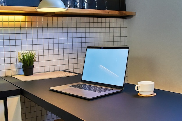 Espace de travail pour le travail en ligne à distance sur un ordinateur portable avec écran blanc vide dans un intérieur loft moderne
