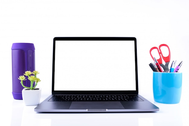 Espace de travail professionnel ou éducatif: ordinateur portable, stylo coloré et ciseaux dans une tasse bleue et haut-parleur violet avec petit arbre vert dans un pot blanc