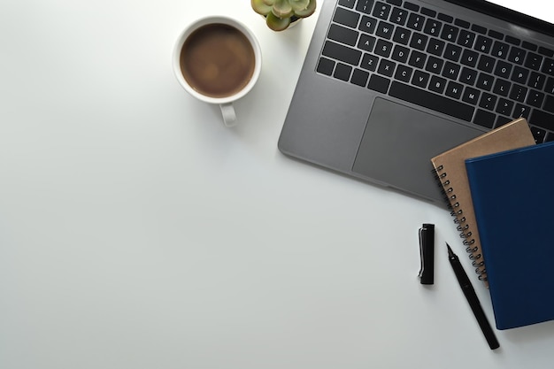 Espace de travail simple avec des livres d'ordinateur portable et une tasse de café sur le bureau blanc Vue de dessus avec espace de flic