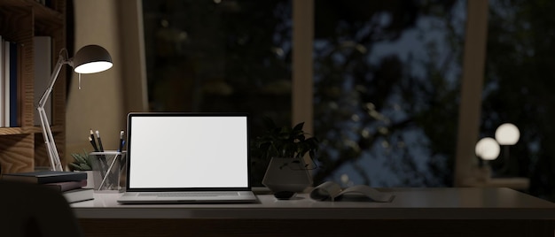 Espace de travail sombre moderne avec papeterie et décor de lampe de table de maquette d'écran blanc d'ordinateur portable