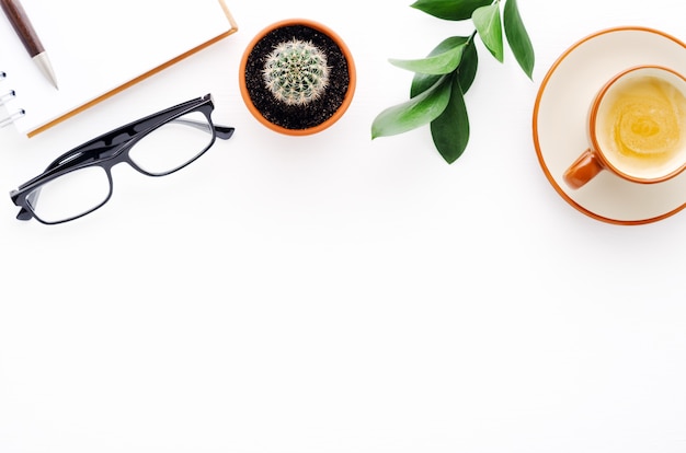 Photo espace de travail avec stylo, cahier, tasse à café, verres et cactus sur fond blanc avec espace copie