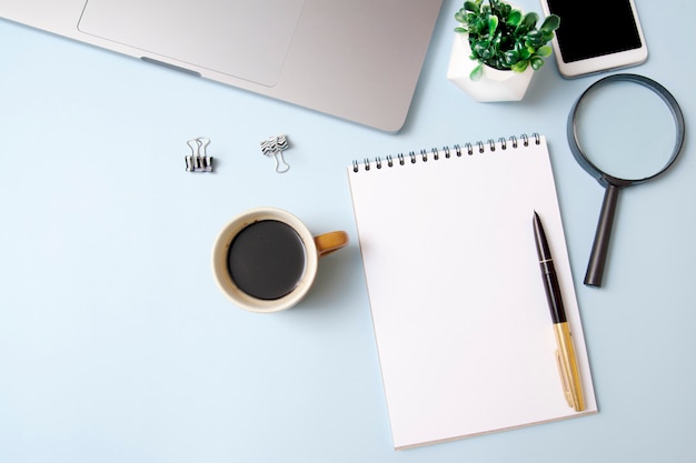 Espace de travail vue de dessus avec une maquette de portable, loupe, café, ordinateur portable sur fond bleu