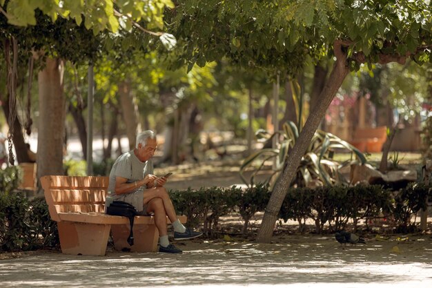 Espagnejuin 29 2022 Un homme âgé est assis sur un banc avec un smartphone dans le parc