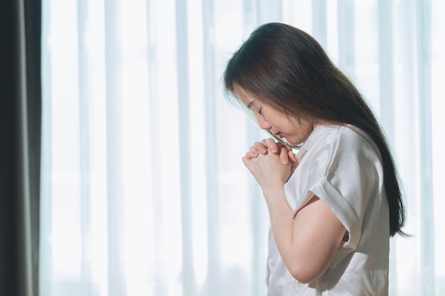 Espoir faire voeu calme asiatique jeune femme croyance main dans la prière assis méditant sur un canapé à la maison Chrétienne priant Dieu pour demander une demande avec les yeux fermés rêvant d'aide merci Dieu