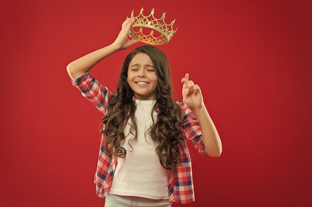 Espoir pour le meilleur Enfant tenant le symbole de la couronne d'or de la princesse Concept d'enfance Chaque fille rêvant de devenir princesse Fille bébé mignon tenir la couronne tout en se tenant sur fond rouge Dame petite princesse