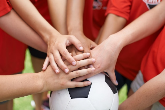 Esprit d'équipe Image recadrée d'un groupe de filles avec leurs mains empilées sur un ballon de football