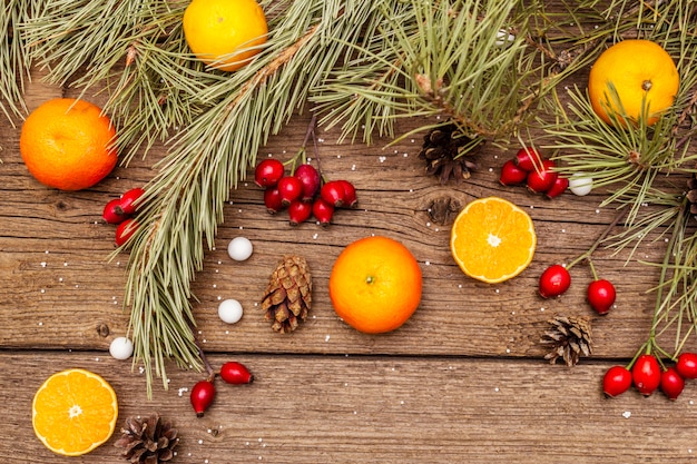 Esprit de Noël sur table en bois. Mandarines fraîches, baies d'églantier, bonbons, branches et pommes de pin, neige artificielle