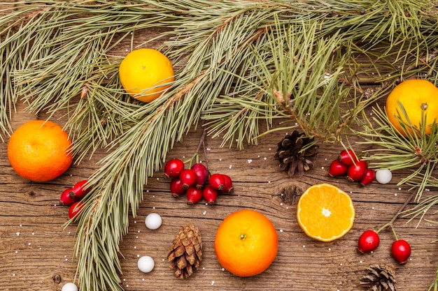 Esprit de Noël sur table en bois. Mandarines fraîches, baies d'églantier, bonbons, branches et pommes de pin, neige artificielle