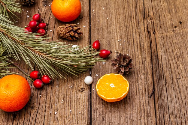 Esprit de Noël sur table en bois. Mandarines fraîches, baies d'églantier, bonbons, branches et pommes de pin, neige artificielle