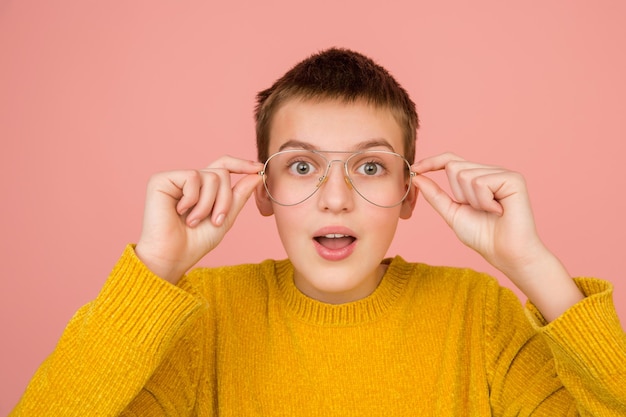 Essayer Des Lunettes. Portrait D'une Fille Caucasienne Sur Fond De Studio Rose Corail Avec Fond Pour L'annonce. Beau Modèle En Pull. Concept D'émotions Humaines, Expression Faciale, Ventes, Publicité, Mode.