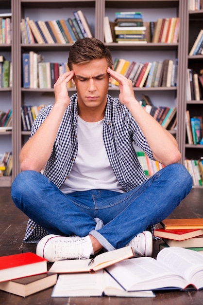 Essayer de se concentrer sur l'étude. Jeune homme frustré touchant sa tête avec les mains et gardant les yeux fermés alors qu'il était assis contre une étagère