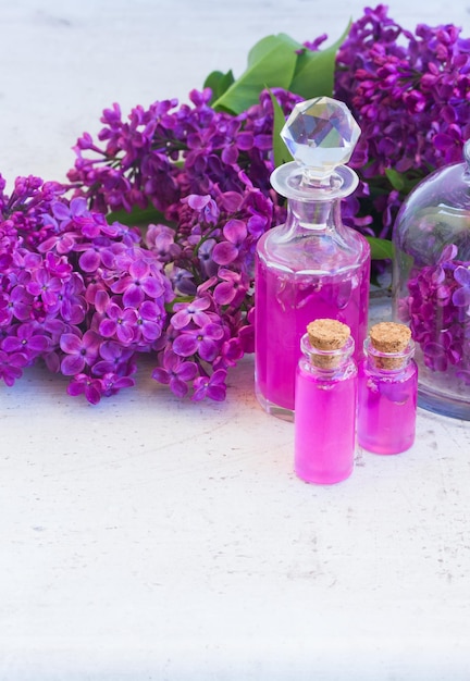 L'essence de lilas dans des flacons de verre et des fleurs de lilas fraîches copient l'espace sur une table en bois