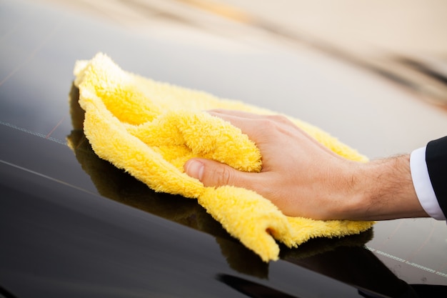 Essuyage du panneau d'une voiture de luxe avec microfibre jaune, vue rapprochée