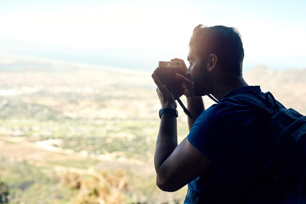 Photo c'est assez magique ici vue arrière d'un jeune homme prenant une photo de la vue panoramique depuis le sommet d'une montagne