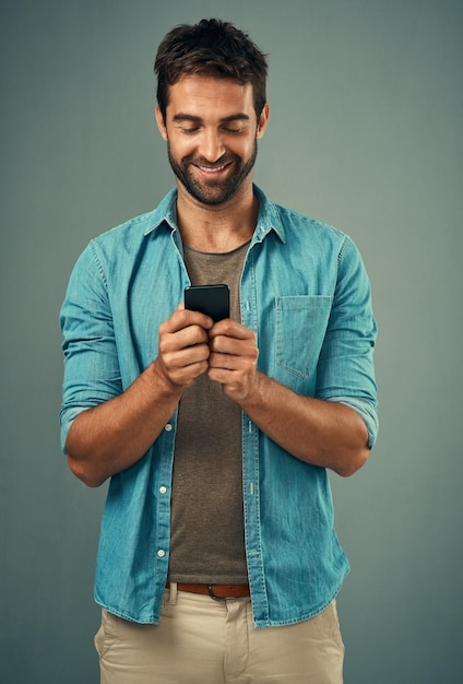 C'est celui avec qui tout le monde veut être en contact Studio photo d'un beau jeune homme utilisant un téléphone portable sur fond gris