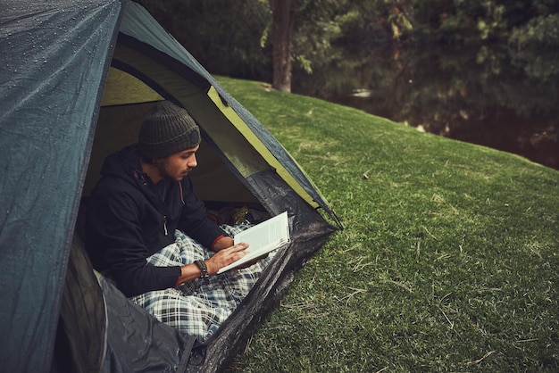 C'est un endroit paisible pour lire Photo d'un jeune homme lisant un livre assis dans sa tente dans un camping