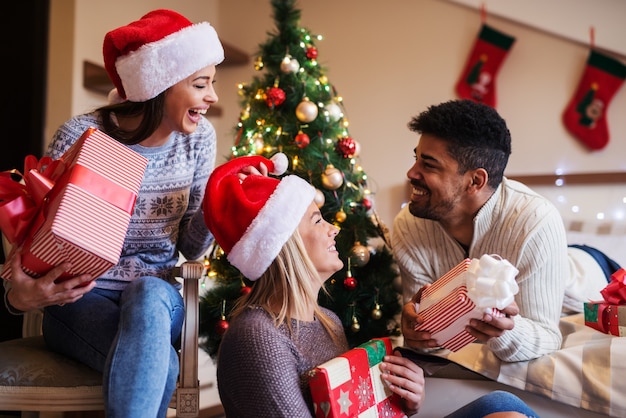 C'est L'heure Des Cadeaux! Groupe De Trois Amis Heureux Partageant Des Cadeaux Du Nouvel An. Assis Dans Une Pièce Avec Une Belle Décoration De Nouvel An.