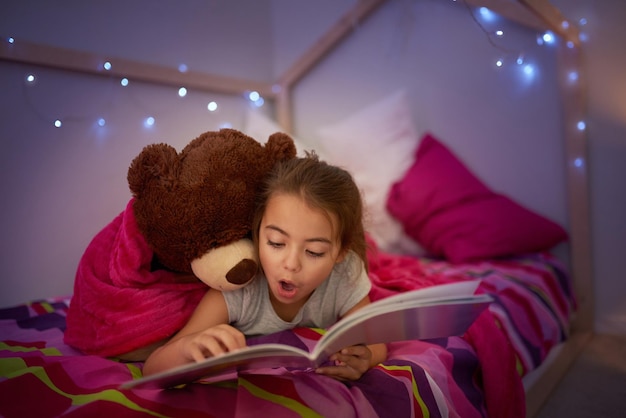 C'est une histoire pleine de merveilleuses surprises Photo recadrée d'une petite fille lisant un livre au lit avec son ours en peluche