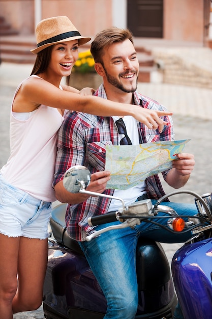 C'est juste là ! Beau jeune homme tenant une carte alors qu'il était assis sur un scooter avec sa belle petite amie debout près de lui et pointant vers l'extérieur