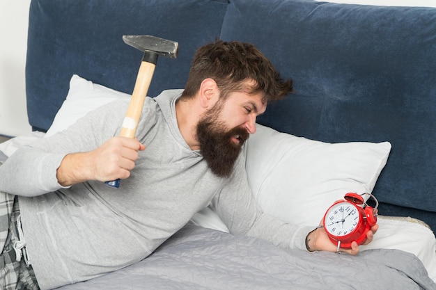 C'est lundi le bruit de la haine du réveil Un gars irrité détruit une horloge ennuyeuse Un homme éveillé mécontent de la sonnerie du réveil Dormir plus longtemps Concept de sommeil sain Un homme barbu hipster veut dormir