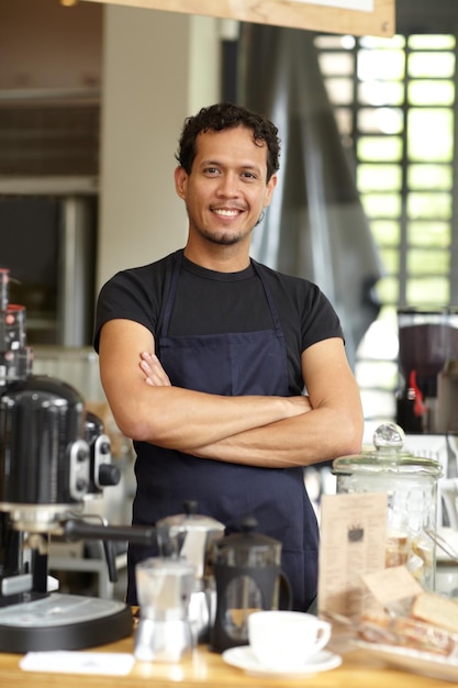 C'est un maître du brassage Photo d'un beau barista debout derrière son café-bar, les bras croisés