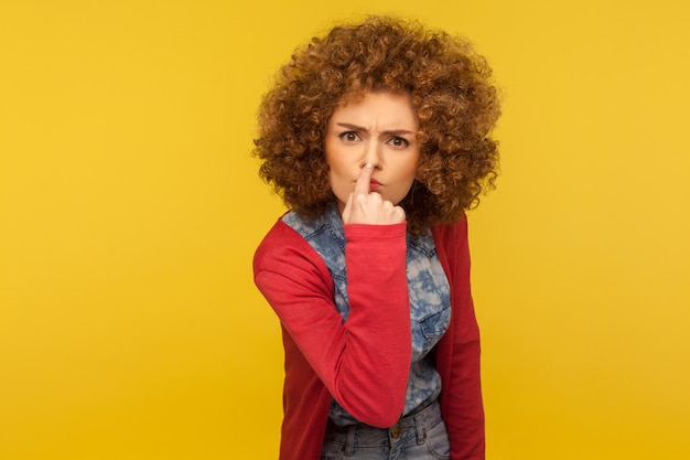 C'est un mensonge. Portrait d'une femme en colère avec des cheveux bouclés moelleux touchant le nez, montrant un geste de menteur, exprimant sa méfiance à l'égard de la fausse suggestion, de la tromperie. studio d'intérieur tourné isolé sur fond jaune