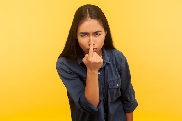 C'est un mensonge Portrait d'une fille suspecte en chemise en jean touchant le nez faisant un geste de menteur langage corporel symbole de tromperie mensonge et tromperie prise de vue en studio intérieur isolé sur fond jaune